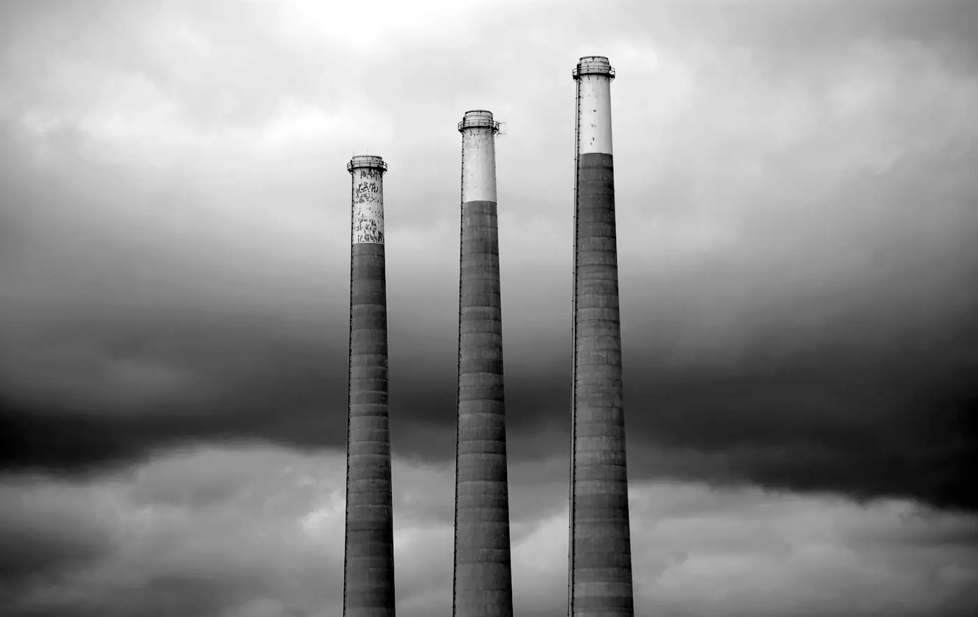 Three tall industrial chimneys against a dark cloudy sky